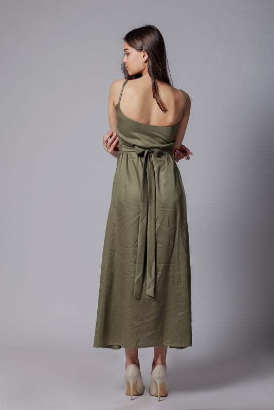 A woman wearing a sleeveless, V-neck, olive green long dress with an adjustable bow at the back, made from a cotton satin blend.