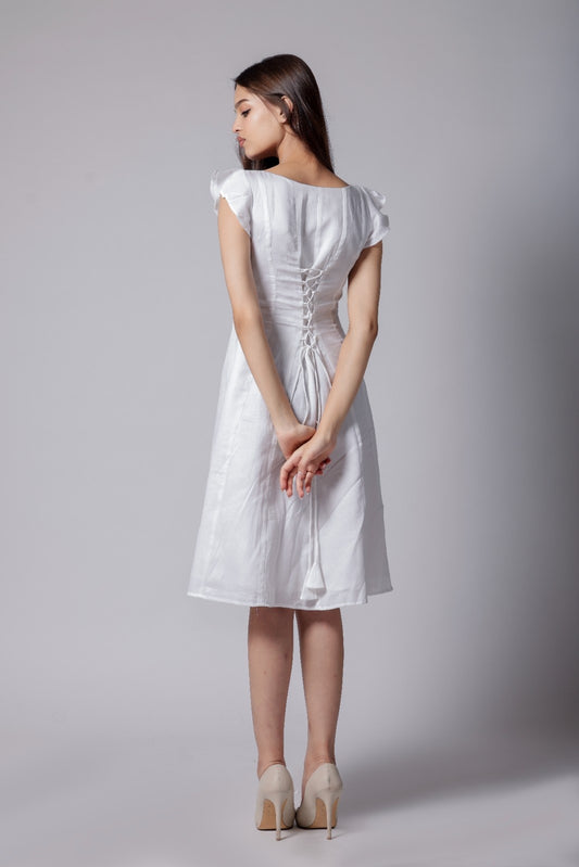 A woman wearing a white knee-length dress with flared sleeves, corset back knots and a sweetheart neckline.