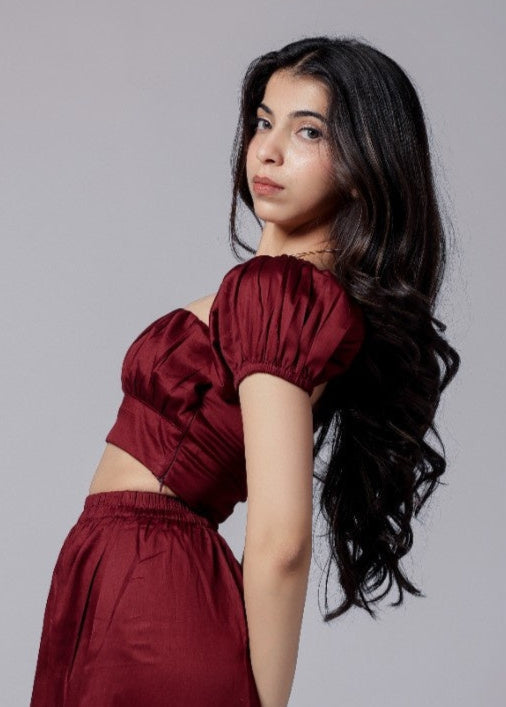 A model wearing a wine-colored skirt set with a crop top and a long skirt with a side slit, with sleek neckline and chic fit.