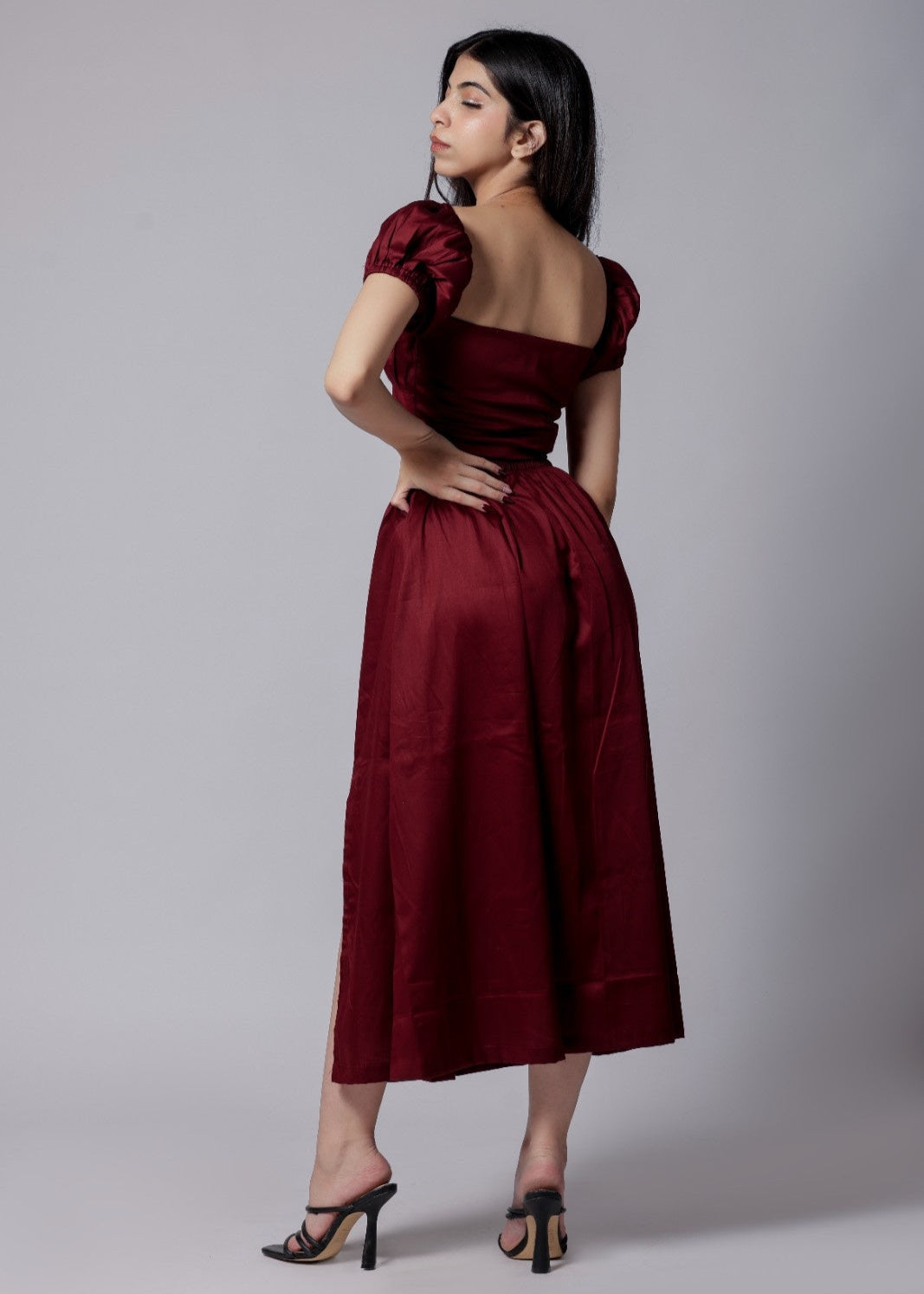 A model wearing a wine-colored skirt set with a crop top and a long skirt with a side slit, with sleek neckline and chic fit.