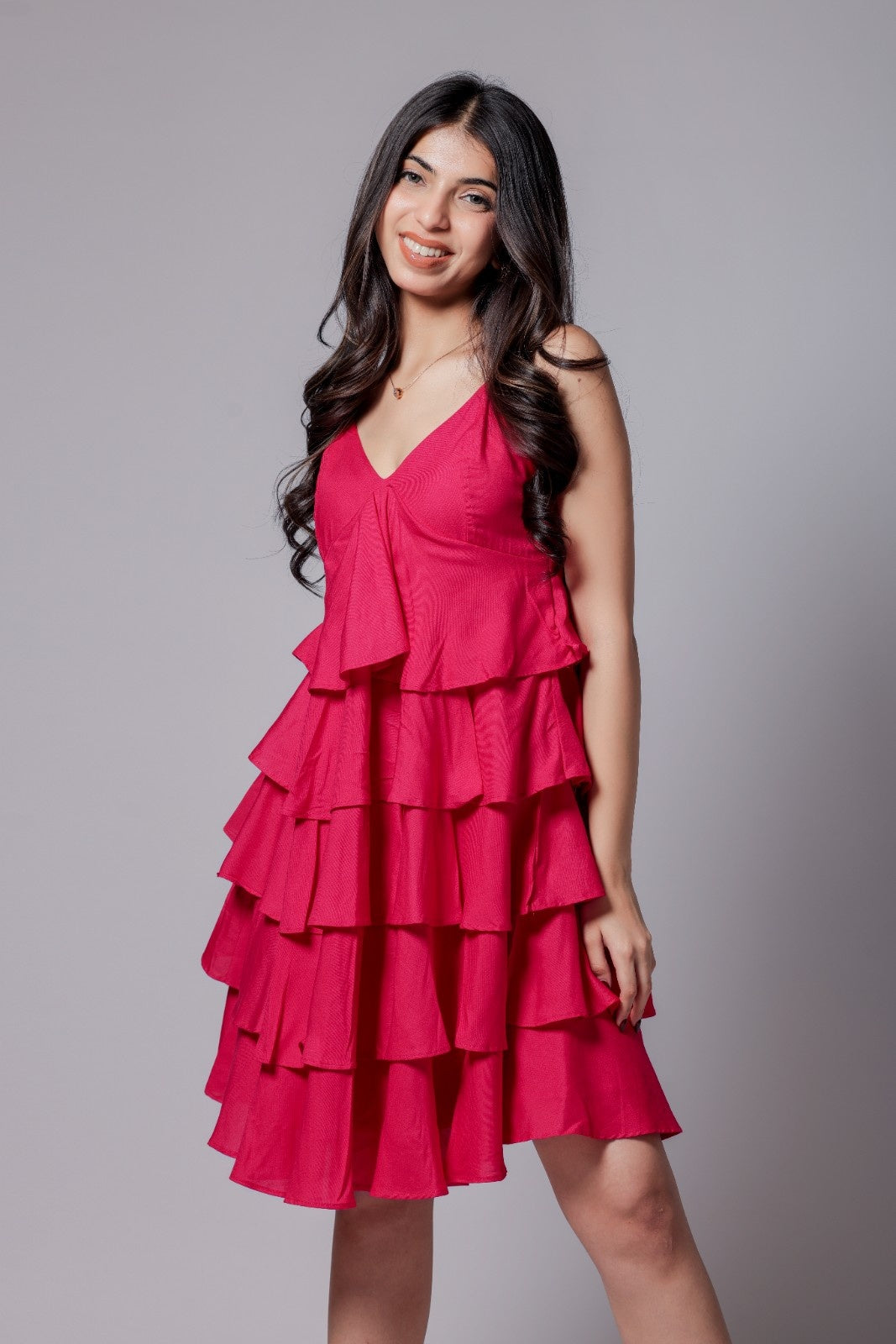 A woman in a bright pink, sleeveless, V-neck, flared mini dress with adjustable straps and an all-over flare design.