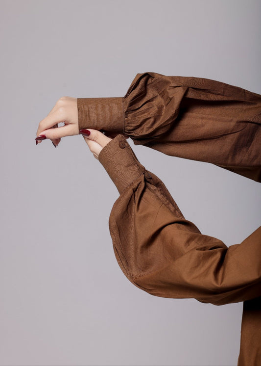 A female wearing a pure cotton brown co-ord set with a gathered tailored shirt and flowy pants.