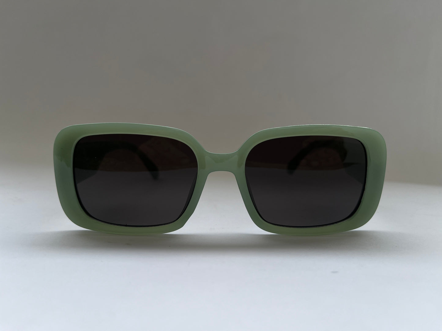 Green sunglasses with dark lenses on a light gray background