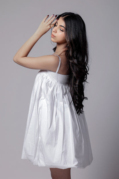 A woman wearing a white, balloon, puffier, sleeveless knee-length dress with adjustable straps.