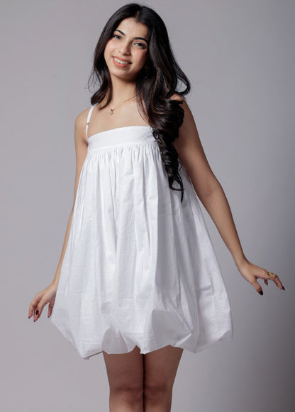 A woman wearing a white, balloon, puffier, sleeveless knee-length dress with adjustable straps.