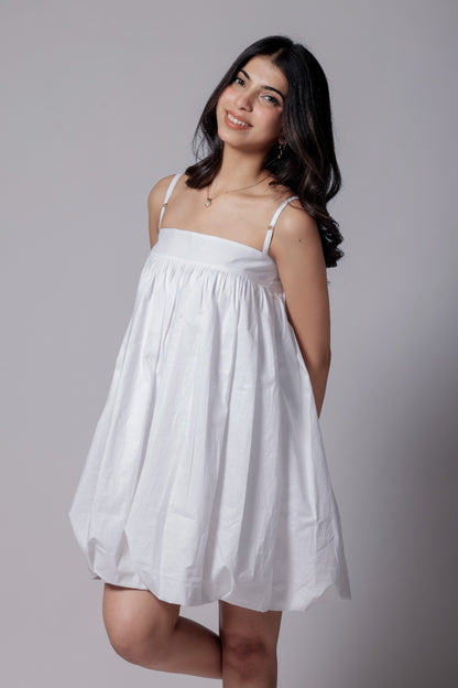 A woman wearing a white, balloon, puffier, sleeveless knee-length dress with adjustable straps.