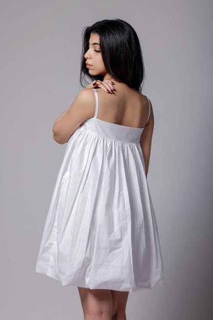 A woman wearing a white, balloon, puffier, sleeveless knee-length dress with adjustable straps.