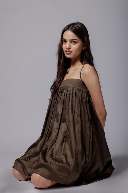 A model wearing a mocha brown, puffier silhouette dress with adjustable straps and a flared design.