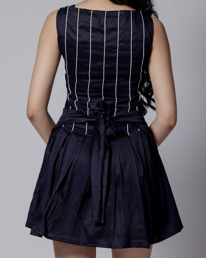 Model in a navy blue sleeveless dress with white piping, flared bottom, and adjustable back bow from Hyghbreed