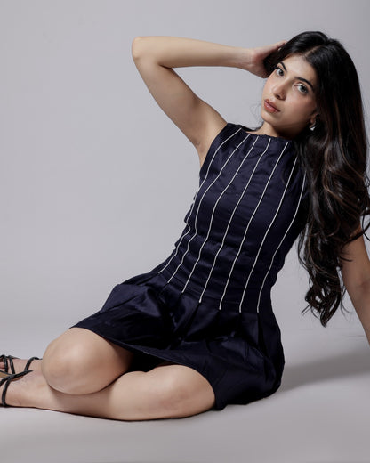 Model in a navy blue sleeveless dress with white piping, flared bottom, and adjustable back bow from Hyghbreed