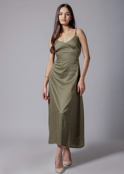 A woman wearing a sleeveless, V-neck, olive green long dress with an adjustable bow at the back, made from a cotton satin blend.