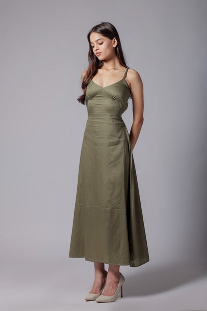 A woman wearing a sleeveless, V-neck, olive green long dress with an adjustable bow at the back, made from a cotton satin blend.