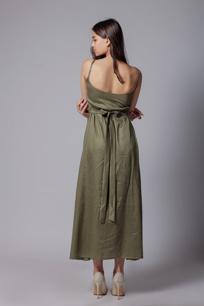 A woman wearing a sleeveless, V-neck, olive green long dress with an adjustable bow at the back, made from a cotton satin blend.