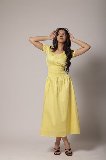 A woman wearing a lemon-yellow cotton long dress with a ruched waist, V-round neckline, and short sleeves.