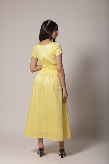 A woman wearing a lemon-yellow cotton long dress with a ruched waist, V-round neckline, and short sleeves.