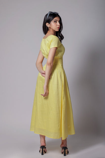 A woman wearing a lemon-yellow cotton long dress with a ruched waist, V-round neckline, and short sleeves.