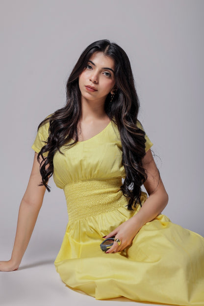 A woman wearing a lemon-yellow cotton long dress with a ruched waist, V-round neckline, and short sleeves.