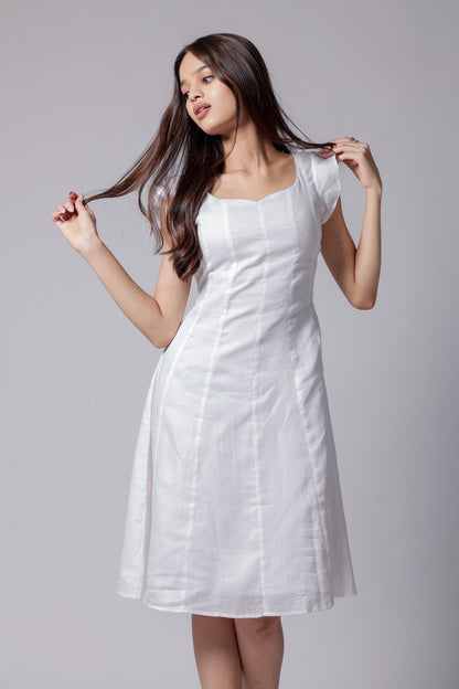 A woman wearing a white knee-length dress with flared sleeves, corset back knots and a sweetheart neckline.