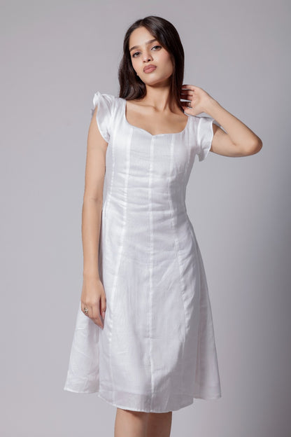 A woman wearing a white knee-length dress with flared sleeves, corset back knots and a sweetheart neckline.