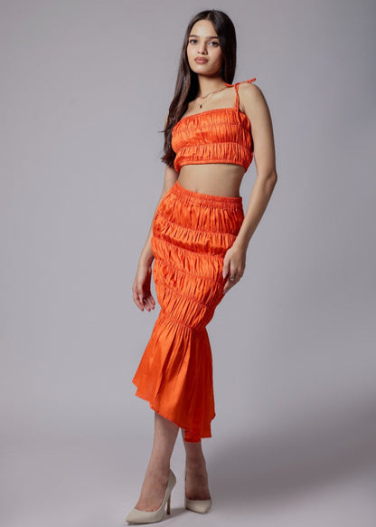 A model wearing a bright orange ruched skirt set with an elasticated top and asymmetrical flare skirt.