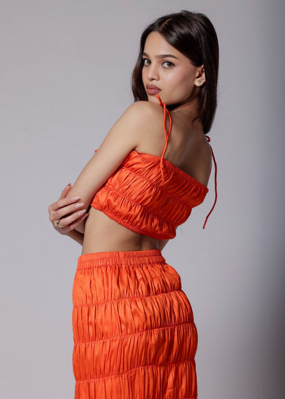 A model wearing a bright orange ruched skirt set with an elasticated top and asymmetrical flare skirt.
