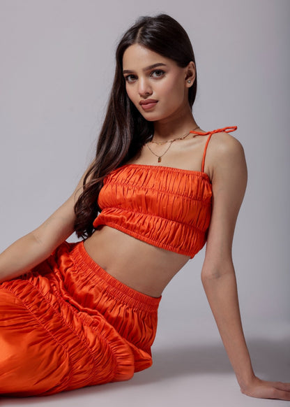 A model wearing a bright orange ruched skirt set with an elasticated top and asymmetrical flare skirt.