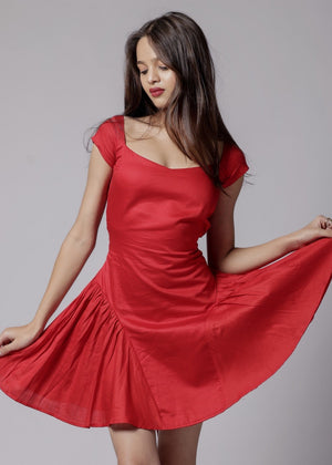 A woman in a red, short-sleeved, square neckline, flared dress with a bow at the back waist and adjustable straps.