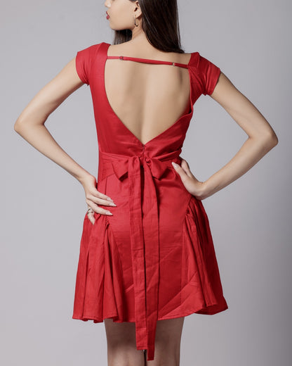 A woman in a red, short-sleeved, square neckline, flared dress with a bow at the back waist and adjustable straps.