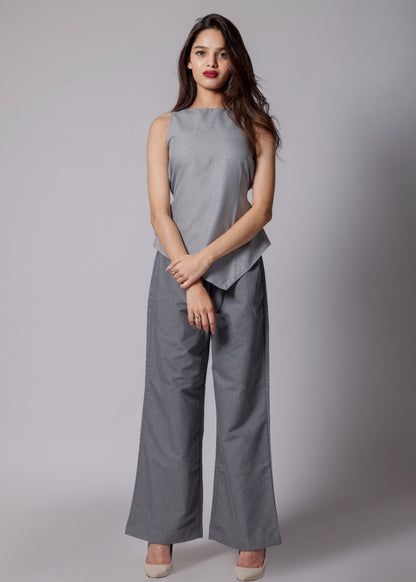A woman wearing terry cotton co-ord set with an asymmetrical sleeveless sleek top in light gray and tailored dark gray pants with pockets. 