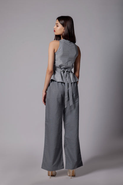 A woman wearing terry cotton co-ord set with an asymmetrical sleeveless sleek top in light gray with back tie up  bow and tailored dark gray pants with pockets. 