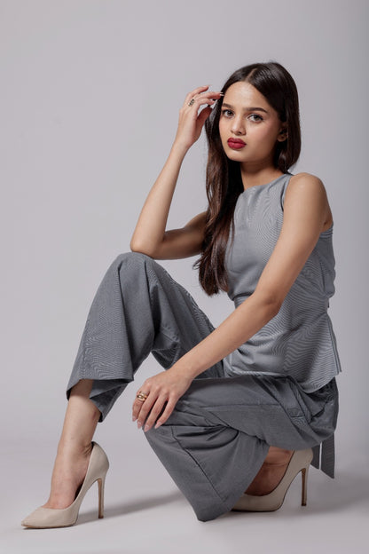 A woman wearing terry cotton co-ord set with an asymmetrical sleeveless sleek top in light gray with back tie up  bow and tailored dark gray pants with pockets. 