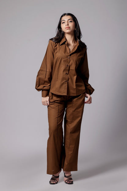 A female wearing a pure cotton brown co-ord set with a gathered tailored shirt and flowy pants.