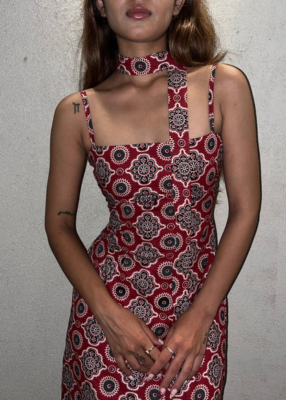 woman wearing a sleeveless red block printed cotton dress and black patterned maxi dress with a high slit, and a corset tie-up back & a neck band.