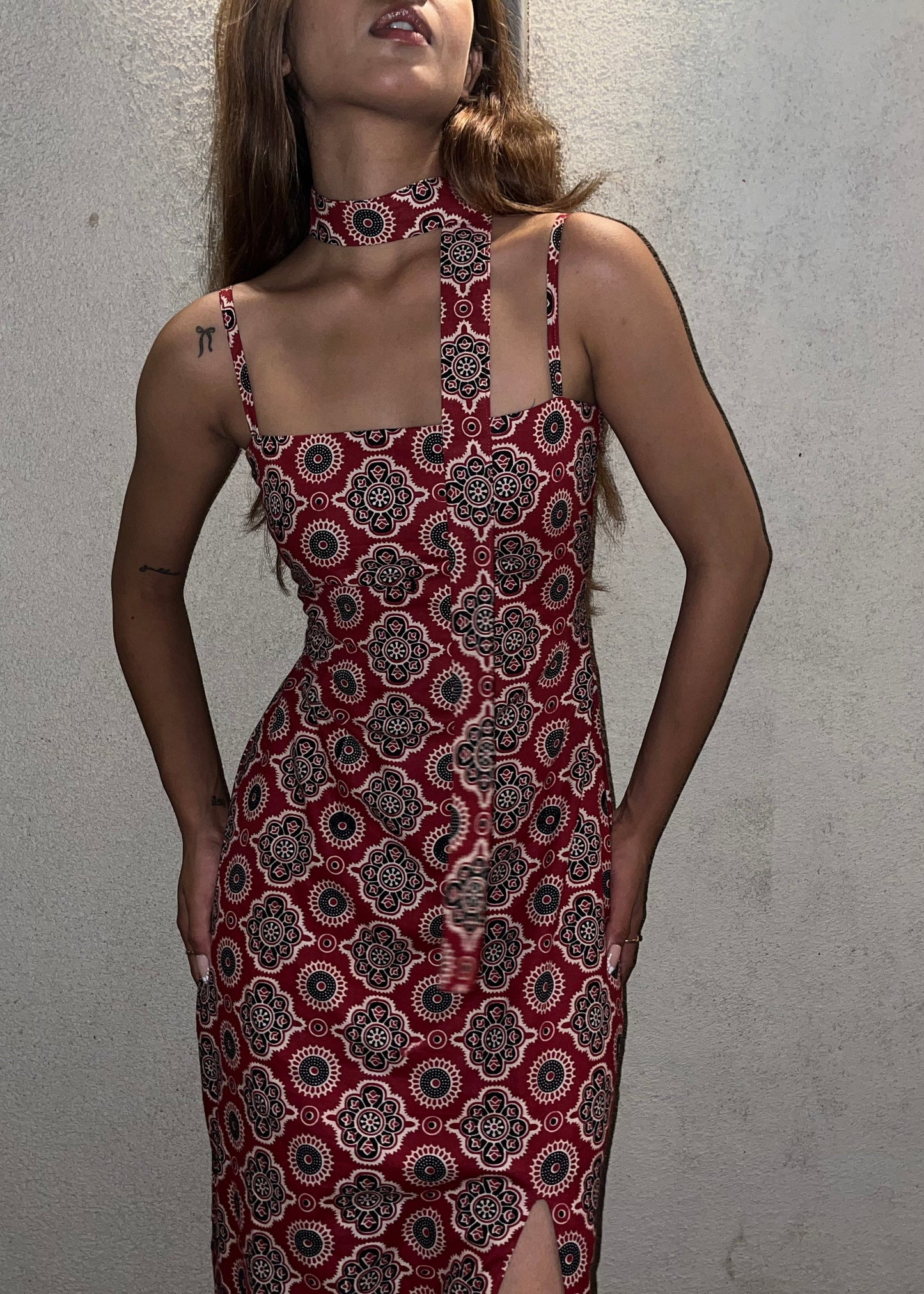 woman wearing a sleeveless red block printed cotton dress and black patterned maxi dress with a high slit, and a corset tie-up back & a neck band.