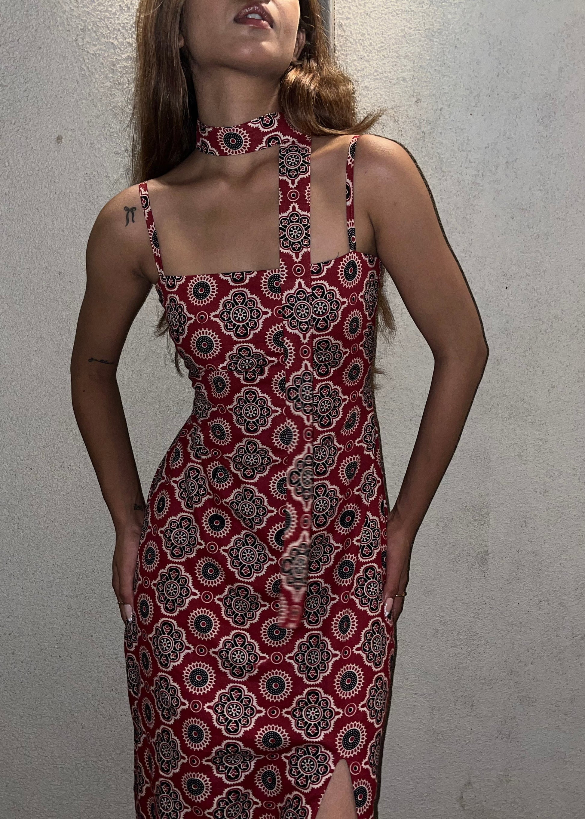 woman wearing a sleeveless red block printed cotton dress and black patterned maxi dress with a high slit, and a corset tie-up back & a neck band.