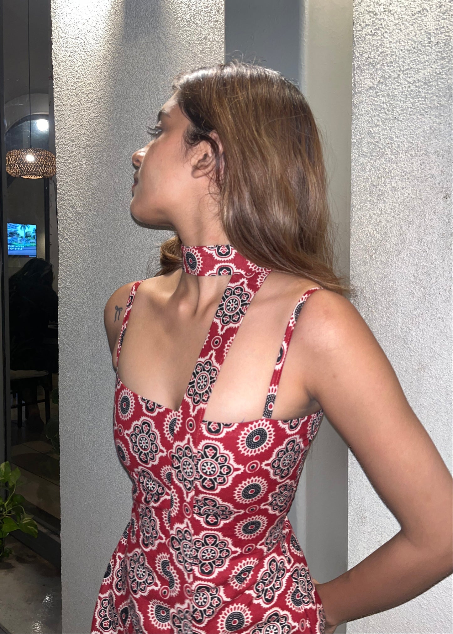 woman wearing a sleeveless red block printed cotton dress and black patterned maxi dress with a high slit, and a corset tie-up back & a neck band.