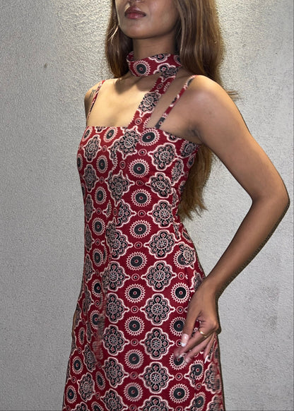 woman wearing a sleeveless red block printed cotton dress and black patterned maxi dress with a high slit, and a corset tie-up back & a neck band.