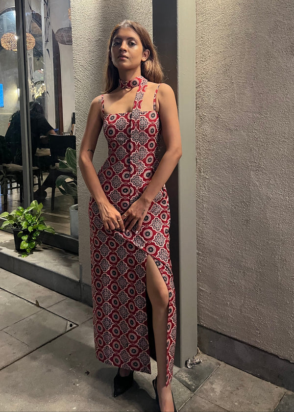 woman wearing a sleeveless red block printed cotton dress and black patterned maxi dress with a high slit, and a corset tie-up back.