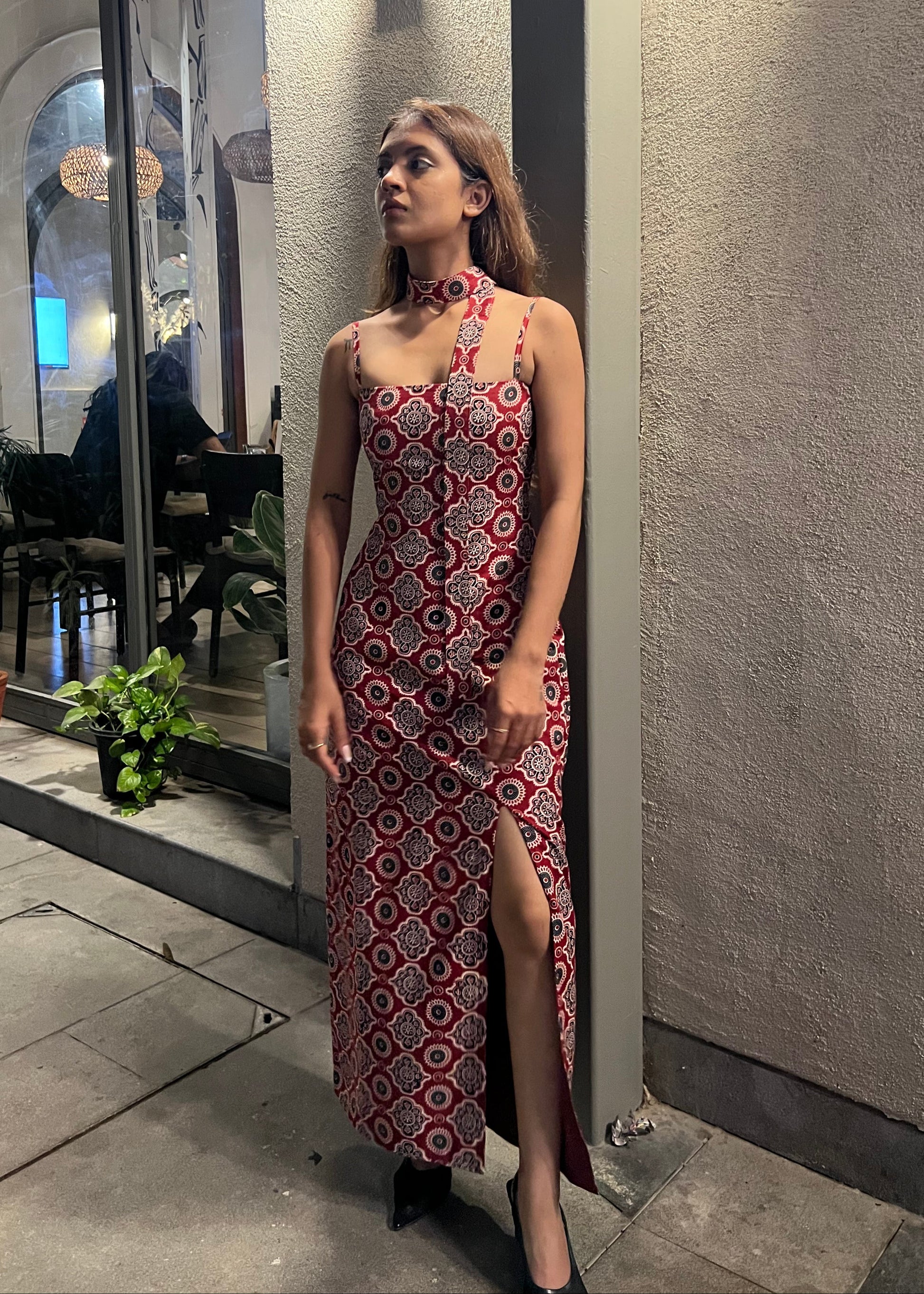 woman wearing a sleeveless red block printed cotton dress and black patterned maxi dress with a high slit, and a corset tie-up back & a neck band.