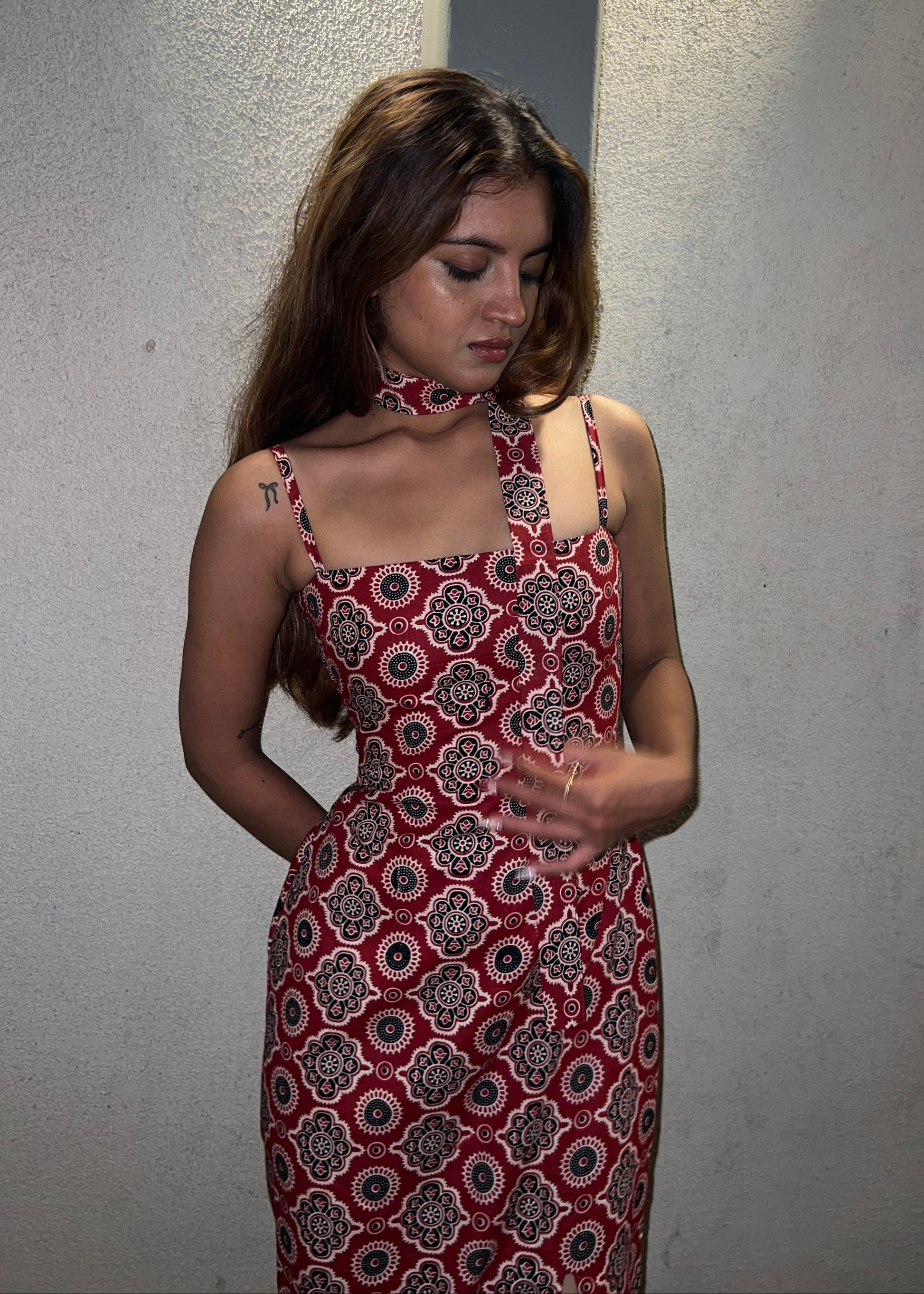 woman wearing a sleeveless red block printed cotton dress and black patterned maxi dress with a high slit, and a corset tie-up back & a neck band.