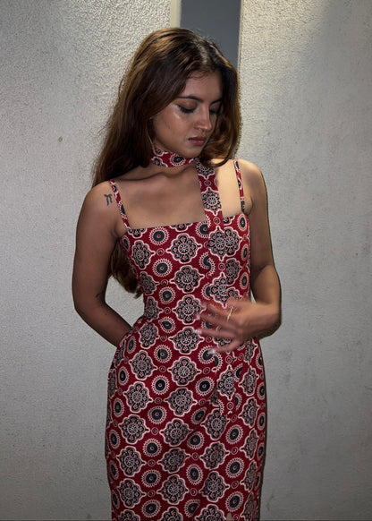 woman wearing a sleeveless red block printed cotton dress and black patterned maxi dress with a high slit, and a corset tie-up back & a neck band.