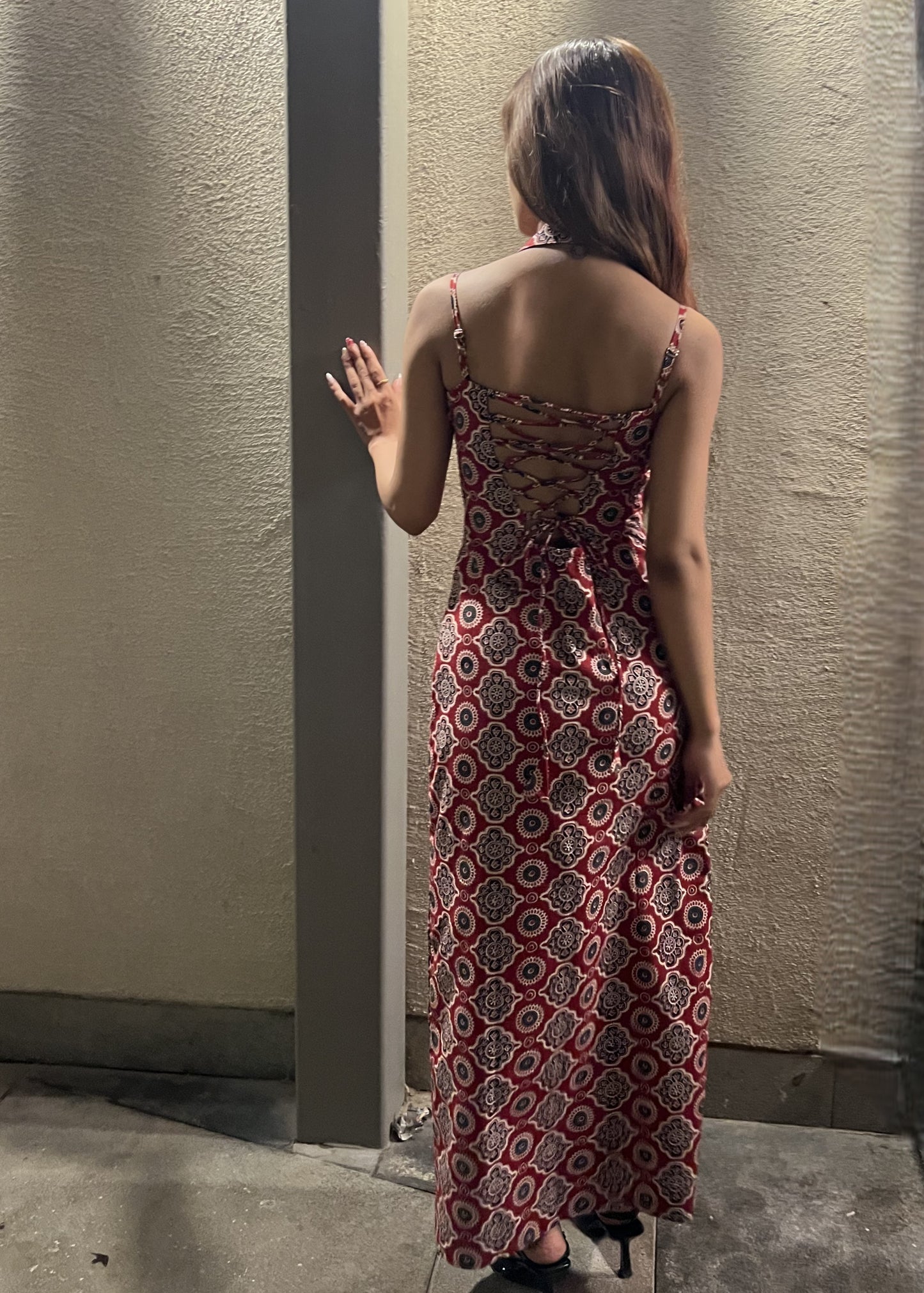 woman wearing a sleeveless red block printed cotton dress and black patterned maxi dress with a high slit, and a corset tie-up back & a neck band. a lace-up open back.