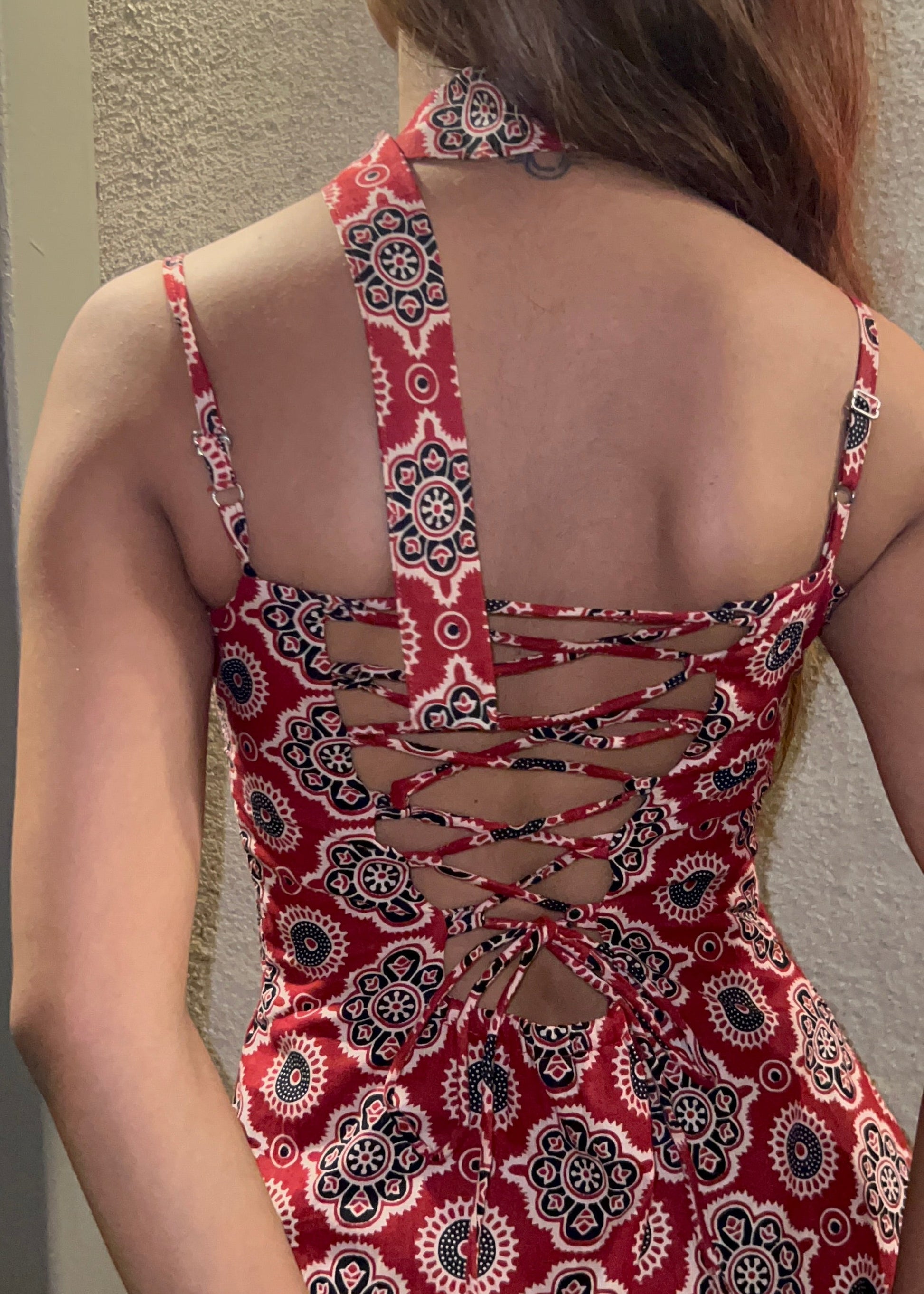 woman wearing a sleeveless red block printed cotton dress and black patterned maxi dress with a high slit, and a corset tie-up back & a neck band.