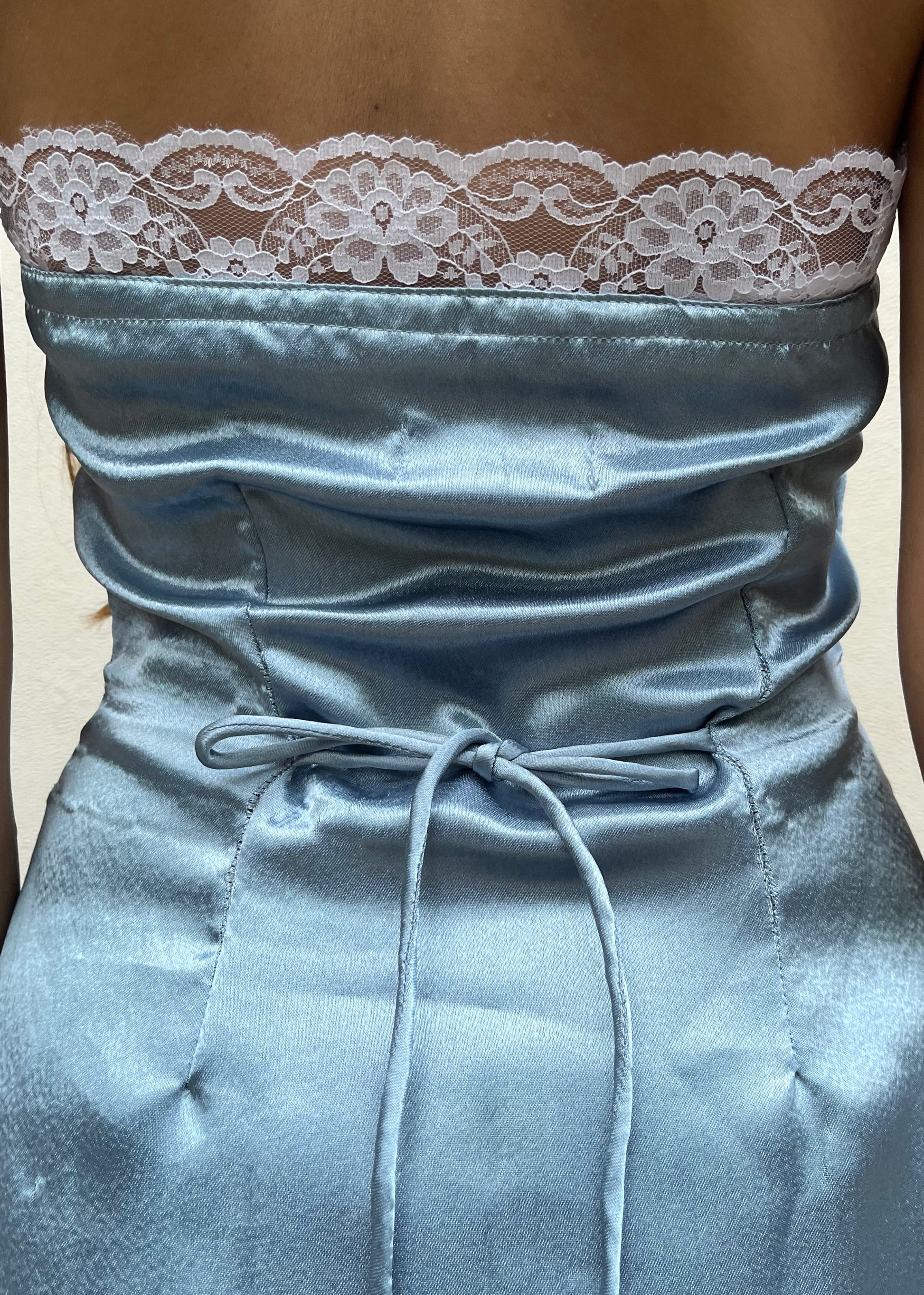 A woman wearing a blue satin halter dress with lace trim, and intricate lace detailing's with side zipper and back tie-up that snatches the waist