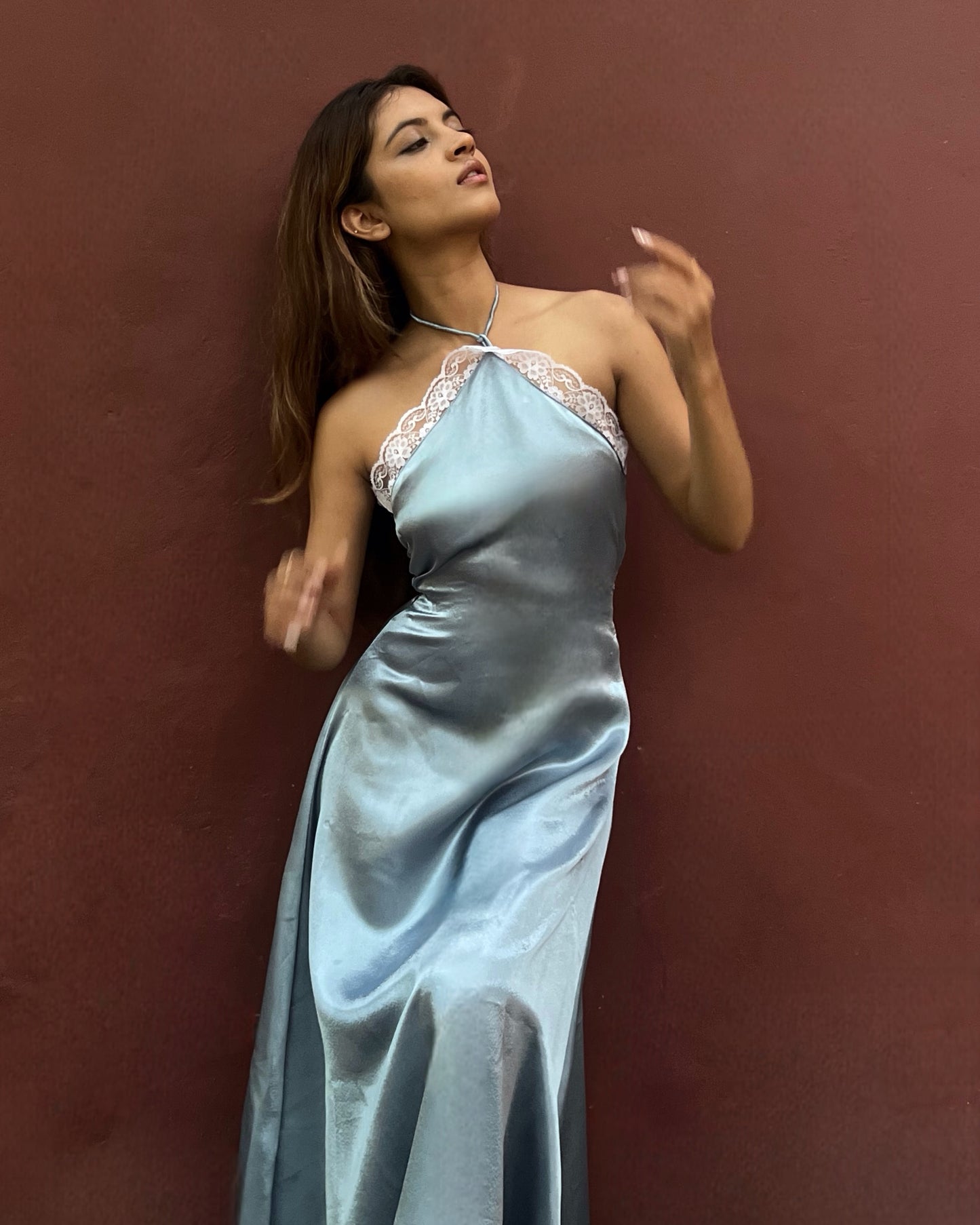 A woman wearing a blue satin halter dress with lace trim, and intricate lace detailing's with side zipper and back tie-up that snatches the waist