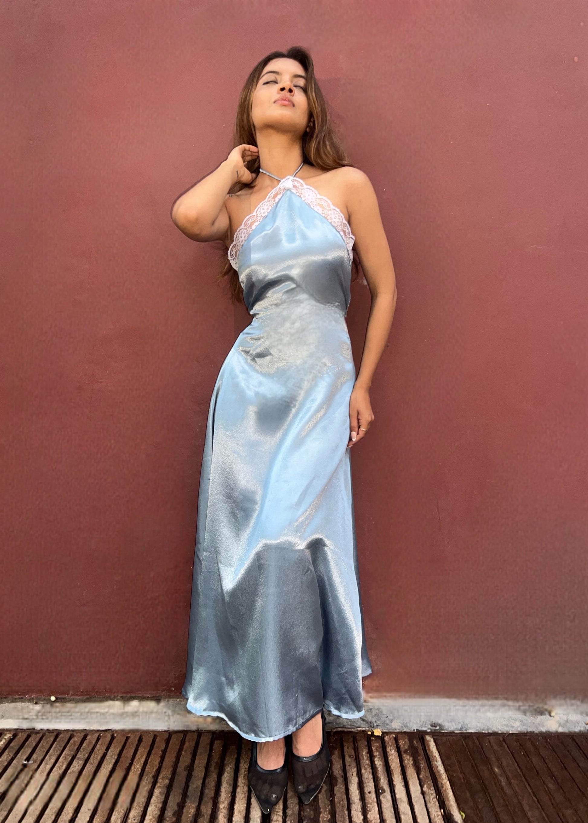 A woman wearing a light blue satin halter-neck maxi dress with white lace trim at the neckline, 